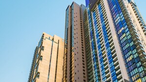 Ein modernes Hochhaus mit einer Mischung aus Glas- und Betonfassaden, einer Tiefgarage darunter und einem kleinen Baum mit rosa Blüten im Vordergrund.