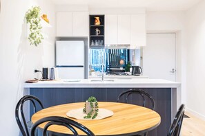 Uma cozinha moderna com armários brancos, uma ilha central e uma área de refeições com mesa de madeira e cadeiras pretas.