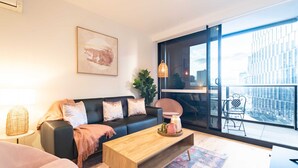 Ein modernes Wohnzimmer mit einer schwarzen Couch, einem Holztisch und einem großen Fenster mit Blick auf die Stadt.