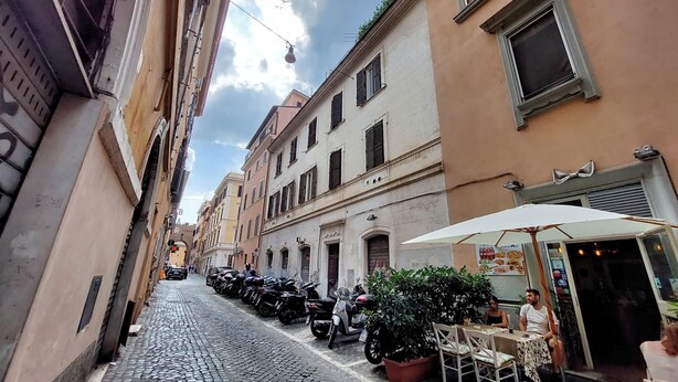 A cobblestone street lined with historic buildings, parked motorcycles, and outdoor seating at a café. - 4bnb - Ombrellari 4 (Rome)