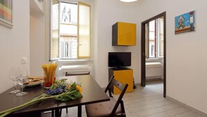 A dining area with a table set for two, a bouquet of flowers, and a window with blinds. - 4bnb - Ombrellari 4 (Rome)