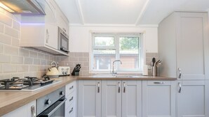A modern kitchen with white cabinetry, a wooden countertop, a built-in oven, a microwave, and a window with blinds. - Fell Foot Lodge (Windermere)