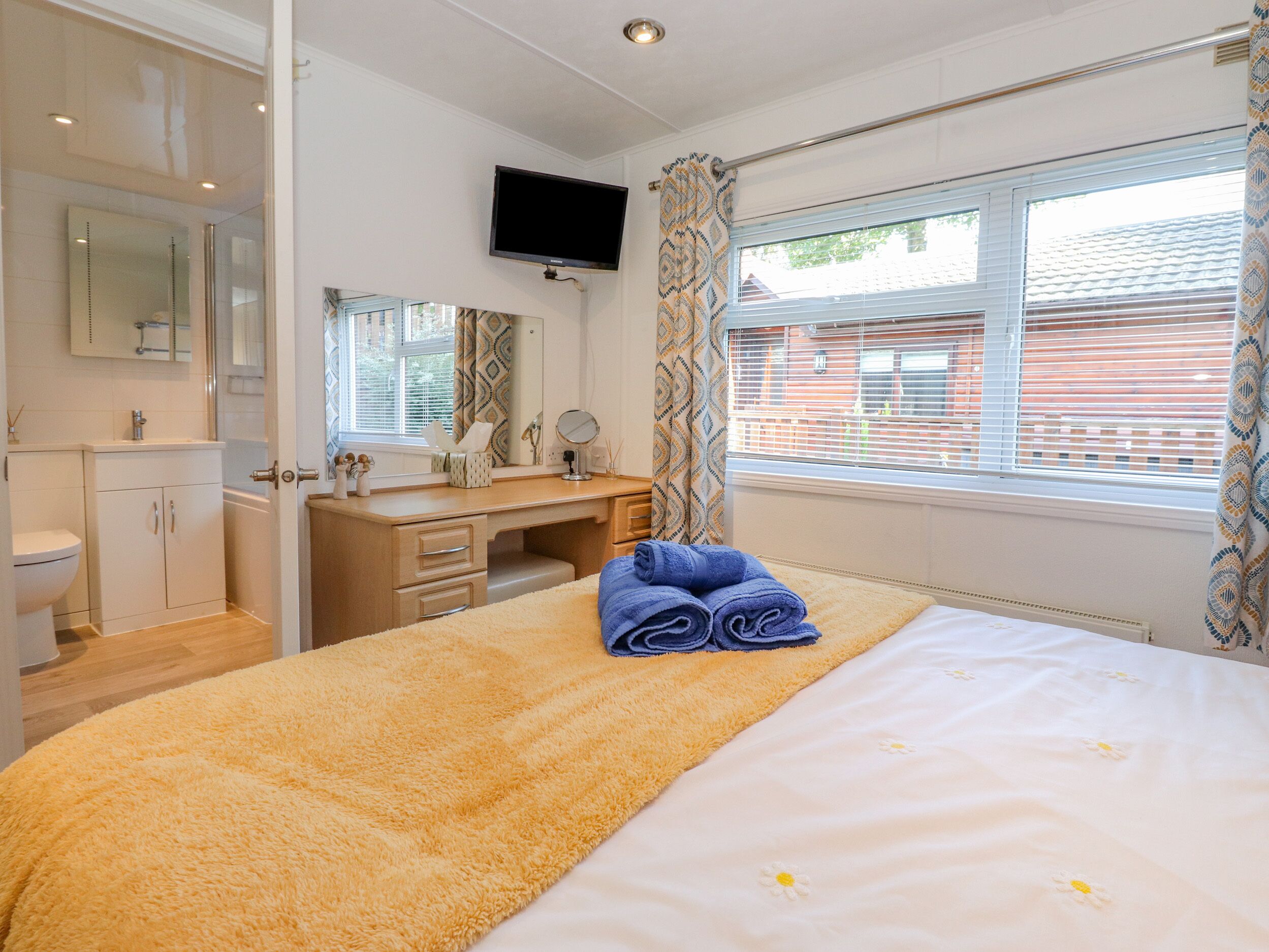 A hotel room with a bed, a desk, a mirror, a television, and a window with curtains.
