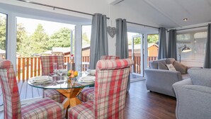 A spacious living area with a glass dining table, plaid chairs, a grey sofa, and a view of the outdoors. - Fell Foot Lodge (Windermere)