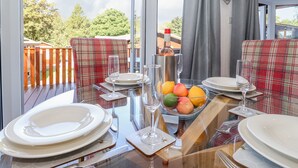 A dining area with a table set for four, featuring plaid chairs, a fruit bowl, and wine glasses. - Fell Foot Lodge (Windermere)
