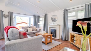 A modern living room with a grey sofa, a wooden coffee table, a flat-screen TV, and a fireplace. - Fell Foot Lodge (Windermere)