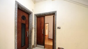 Ein Flur mit zwei Holztüren, eine davon mit einem runden Lüftungsgitter, und einem gefliesten Boden, der in einen weiteren Raum führt.