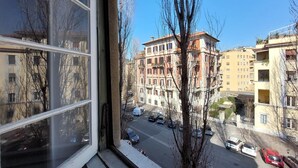 Blick aus einem Fenster auf eine Straße mit parkenden Autos und mehrstöckigen Gebäuden.