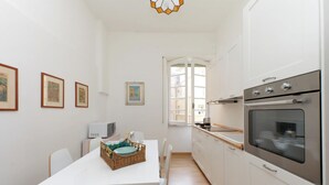 Eine moderne Küche mit weißen Schränken, einem Edelstahlbackofen und einem Essbereich mit weißem Tisch und Stühlen.