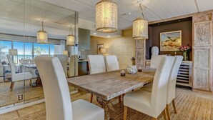 Un comedor con mesa de madera, sillas blancas y lámparas colgantes.