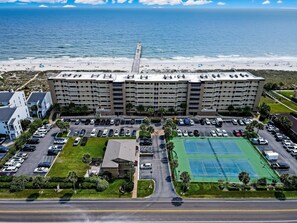 Un hotel de varios pisos con vista a la playa, estacionamiento y canchas de tenis.