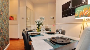 A dining area with a table set for four, including plates, cutlery, and glasses. There is a vase with flowers on the table, and the room has a modern design with a clock on the wall and a decorative lamp. - 4bnb - Otranto Vatican Apartment (Rome)