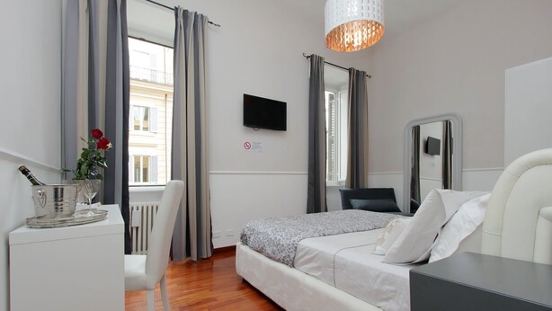 A modern hotel room with a bed, a desk with a computer, a TV, and a window with curtains. - 4bnb - Otranto Vatican Apartment (Rome)