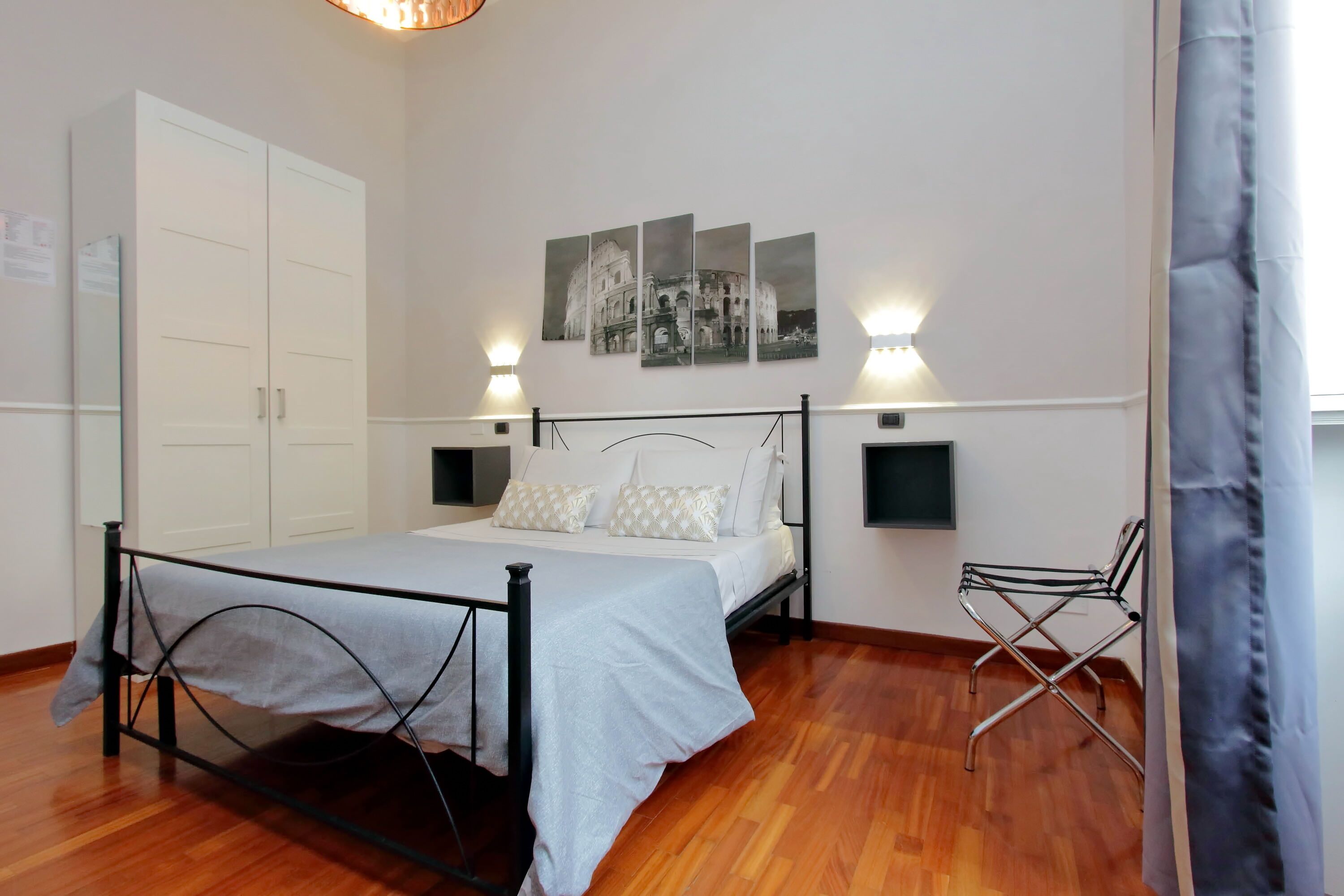 A bedroom with a bed, a wardrobe, a chair, and wall-mounted lights.