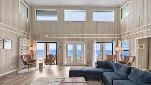A spacious living room with a large sectional sofa, a coffee table, and two armchairs. There are three large windows providing natural light and a view of the outdoors. - Spectacular Gulf Front 30A! Private Pool & Gulf Views, Fall Specials! (Santa Rosa Beach)
