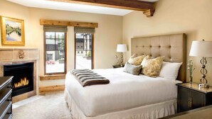 Un dormitorio con una cama grande, una chimenea, un ventanal con vistas y techo de madera.