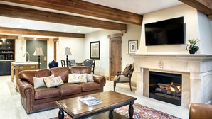 Una sala de estar con chimenea, sofá de cuero, vigas de madera y televisión.