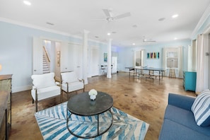 A spacious living room with a large table, a blue sofa, and a patterned rug. - 30A Paradise! Pool, Tiki Bar & 6-Seat Golf Cart 5-Bed Book Now for Fall! (Santa Rosa Beach)
