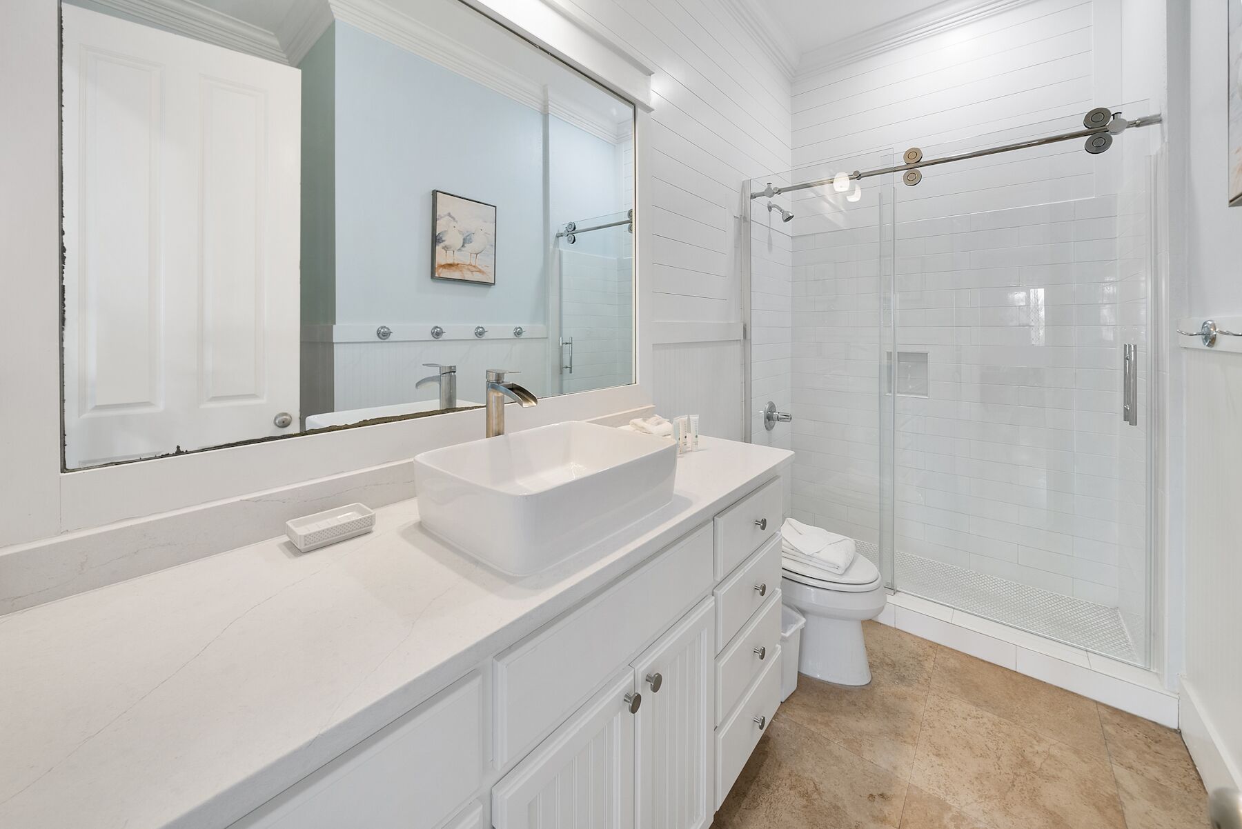 Een moderne badkamer met een grote spiegel, een waskom, een toilet en een douche met glazen wanden.
