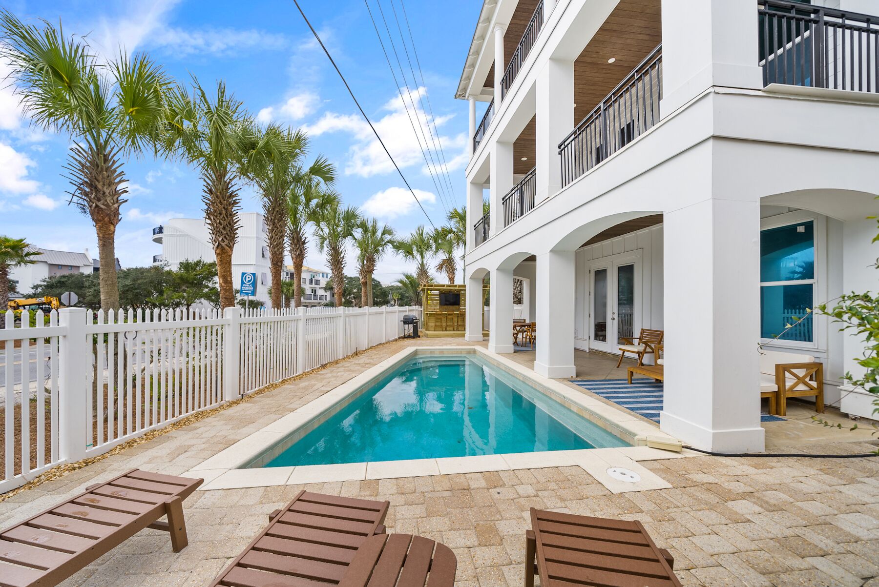 A pool area with lounge chairs, a white fence, and palm trees.