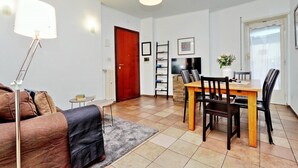 Een woonkamer met een bank, een salontafel, een eettafel met stoelen, een televisie en een lamp.
