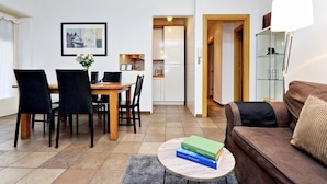 Een moderne woonkamer met een eethoek, een bank, een salontafel met boeken en een keuken op de achtergrond.