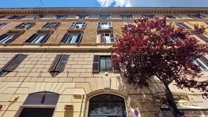 Un edificio a più piani con uno stile architettonico classico, caratterizzato da un ingresso centrale con un cancello in metallo decorato e una serie di finestre con persiane.