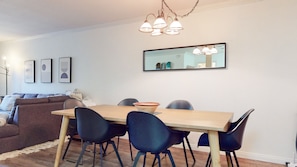 A dining area with a wooden table, four chairs, a bowl, a sofa, and a mirror on the wall.