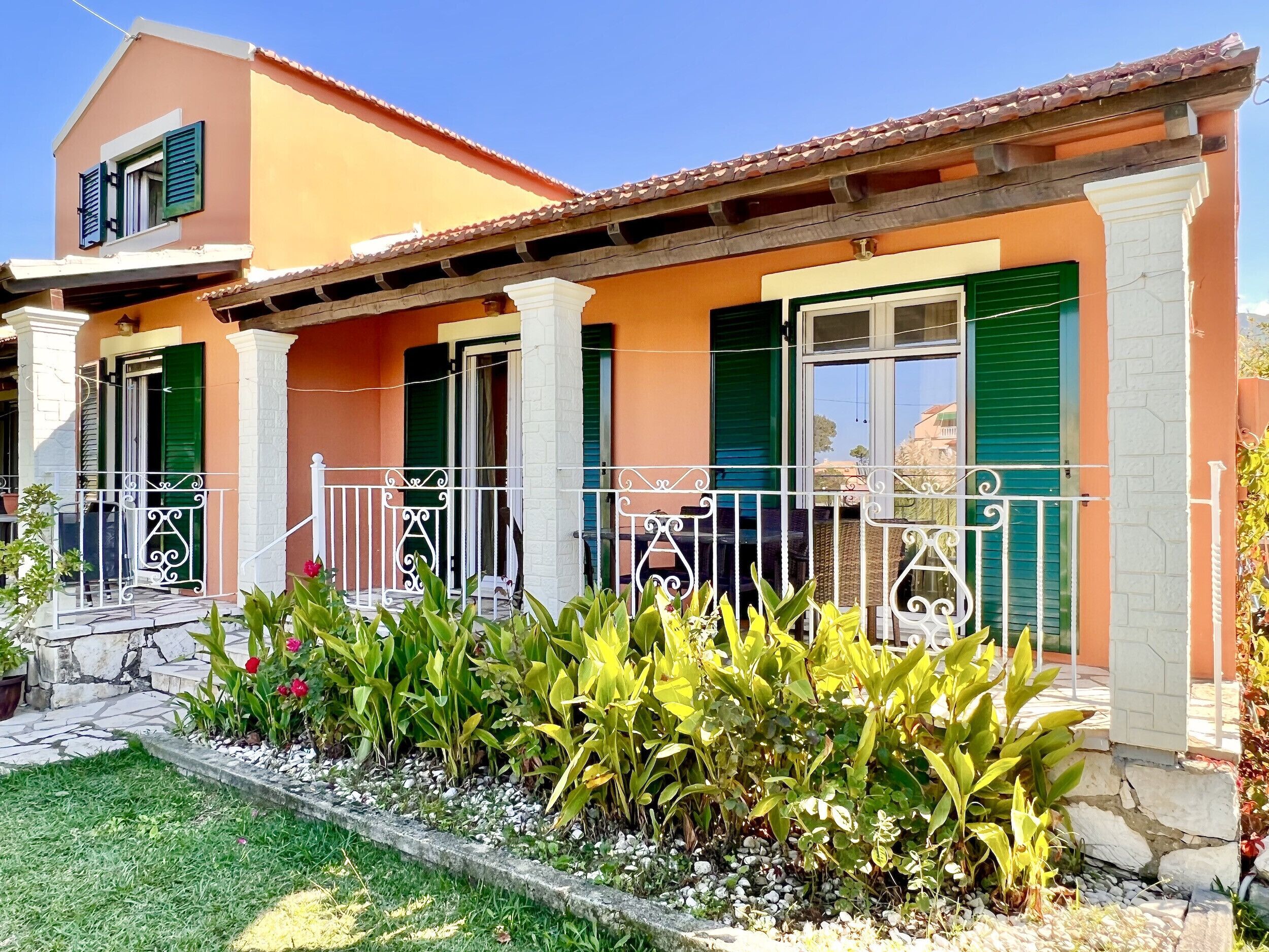 A two-story house with a balcony, green shutters, and a garden in front.