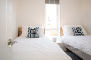 Una habitación con dos camas, ropa de cama blanca y almohadas estampadas.
