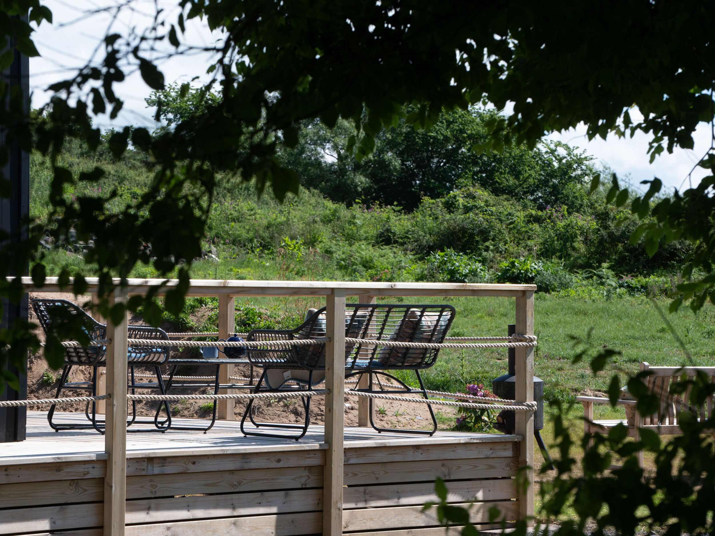 A wooden deck with metal chairs and a rope railing.