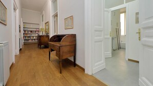A hallway with wooden flooring, white walls, and a wooden desk. There are bookshelves and a door leading to a bathroom. - 4bnb - Spacious Belli Apartment (Rome)