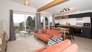 A modern living room with a sofa, a dining table, and a kitchen area with a microwave and oven. - Murmur y Coed (Llanfairpwllgwyngyll)