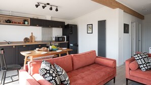A modern kitchen with dark cabinets, a wooden countertop, and a dining area with a red sofa and a table. - Murmur y Coed (Llanfairpwllgwyngyll)