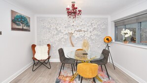 A dining area with a round glass table, four chairs, a colorful rug, a chandelier, and a wall mural.