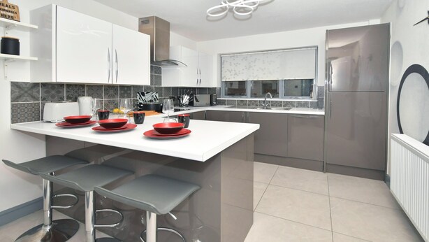 A modern kitchen with white cabinets, a central island with stools, a built-in oven, and a stainless steel refrigerator.