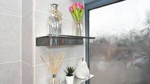 A bathroom with a glass shelf holding a glass bottle, a small potted plant, and a white vase.