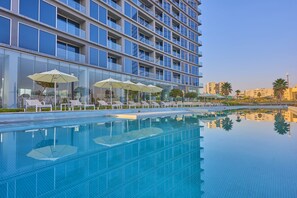 Un hôtel moderne doté d’une piscine, de chaises longues et de parasols.