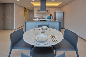 Un espace repas moderne avec une table ronde dressée pour quatre personnes, une cuisine en arrière-plan et une porte sur la gauche.