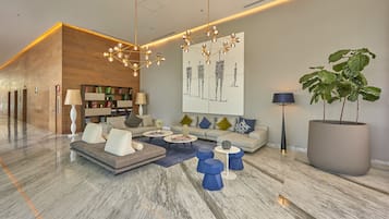 Een moderne lobby met een houten receptiebalie, een zithoek met een bank en salontafels, een groot abstract schilderij en een potplant.