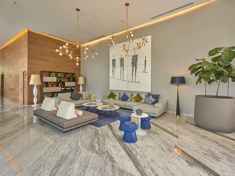 Een moderne lobby met een houten receptiebalie, een zithoek met een bank en salontafels, een groot abstract schilderij en een potplant.