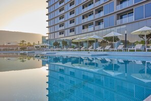 Un hôtel moderne doté d’une piscine, de chaises longues et de parasols.
