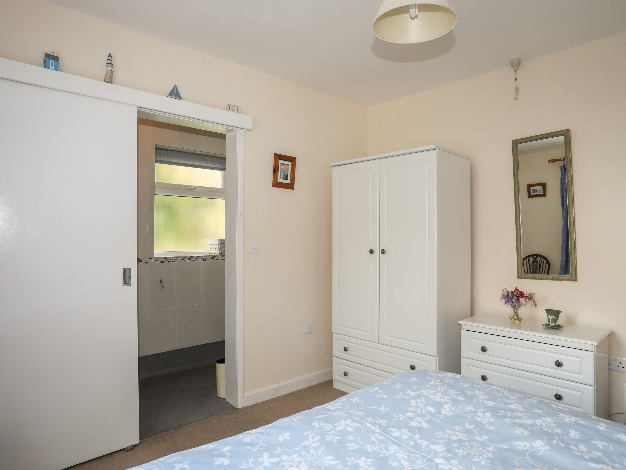 A bedroom with a bed, a wardrobe, a dresser, a mirror, and a door leading to a bathroom.