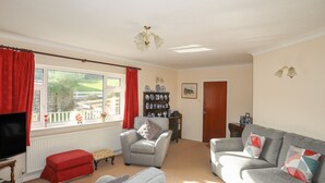Een woonkamer met een bank, fauteuil en poef, een televisie en een raam met uitzicht op een tuin.
