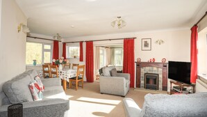 Een woonkamer met een open haard, een televisie en een eethoek met een tafel en stoelen.
