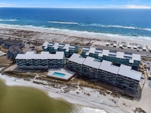 Vista aérea de un hotel costero con varias edificaciones, una piscina y una playa al fondo.