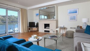 Ein modernes Wohnzimmer mit großem Fernseher, Kamin und Seeblick.