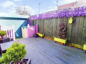 Enjoy a serene outdoor space with a wooden deck, potted plants, and a birdhouse, surrounded by a building.