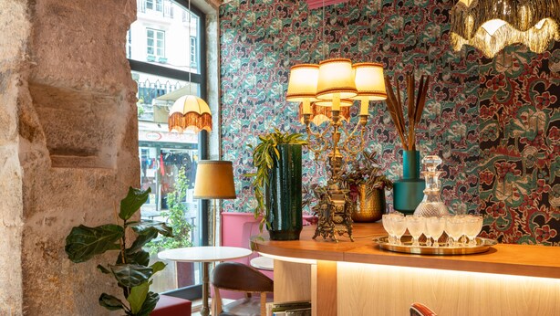 Een bar met een houten toonbank, een bloempot, een decoratieve lamp en behang met een patroon.