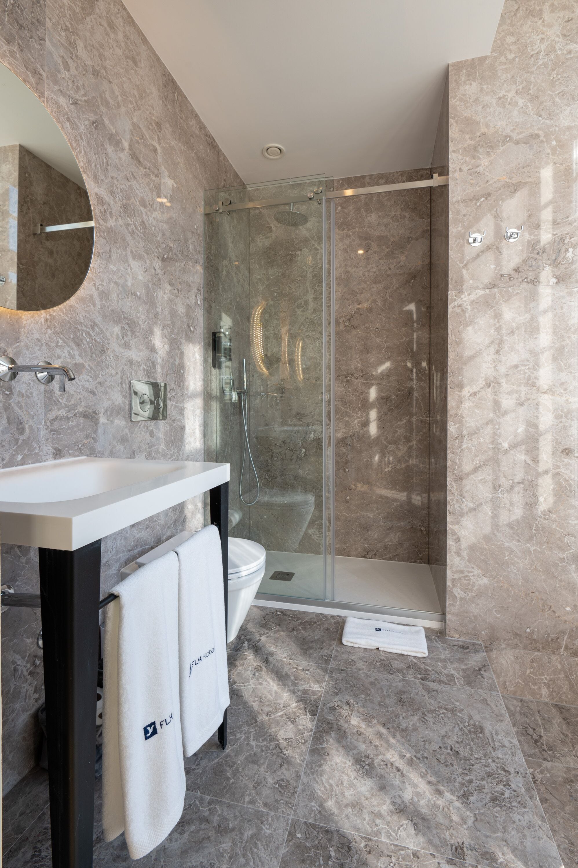 Un baño moderno con lavamanos de mármol, cabina de ducha con vidrio y un inodoro.